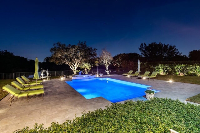 pool at night with a fenced backyard, a pool with connected hot tub, and a patio area