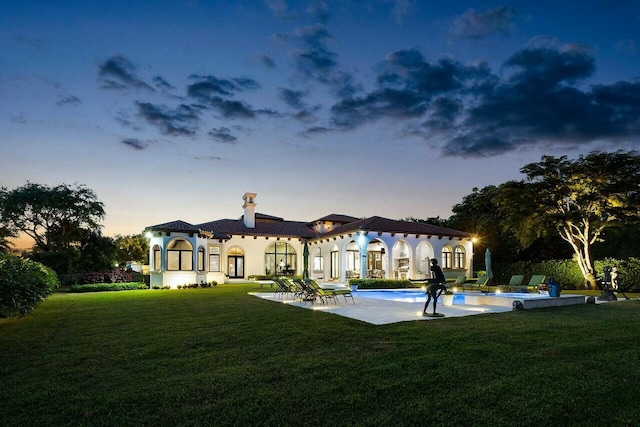 back of property at dusk with an outdoor pool, a patio, stucco siding, and a lawn