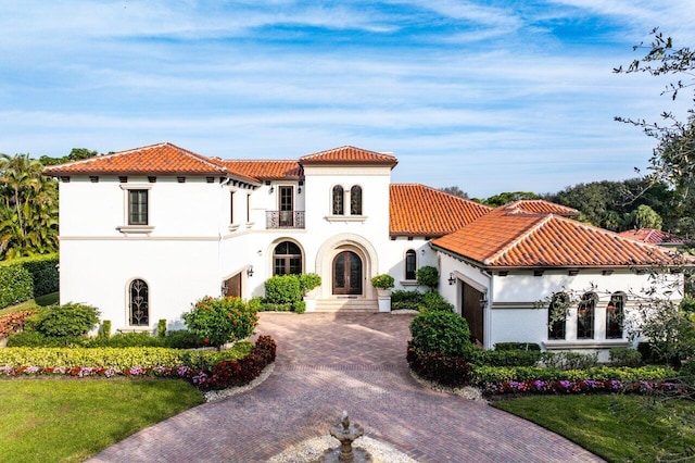 mediterranean / spanish house with stucco siding, an attached garage, a tiled roof, and decorative driveway
