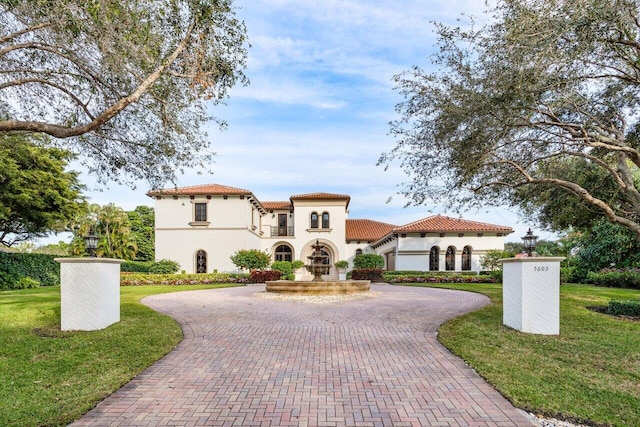 mediterranean / spanish-style home featuring stucco siding, a tile roof, a front lawn, and curved driveway