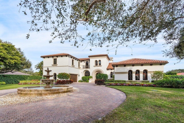 mediterranean / spanish house featuring a garage, a tile roof, a front lawn, stucco siding, and curved driveway