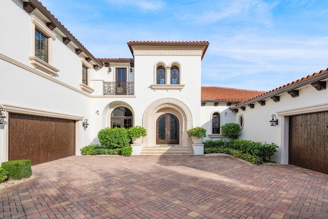 mediterranean / spanish-style home featuring stucco siding, french doors, a tiled roof, a balcony, and decorative driveway