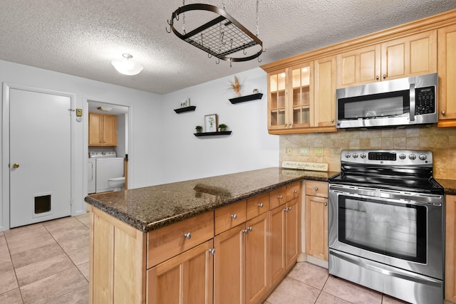 kitchen with appliances with stainless steel finishes, separate washer and dryer, decorative backsplash, kitchen peninsula, and dark stone counters