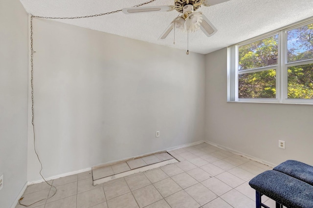 empty room with a textured ceiling, ceiling fan, light tile patterned flooring, and baseboards