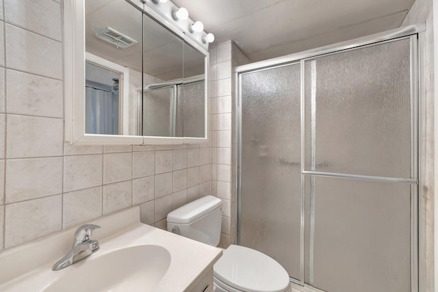 bathroom featuring tile walls, visible vents, toilet, a stall shower, and vanity