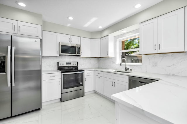 kitchen featuring appliances with stainless steel finishes, white cabinetry, sink, decorative backsplash, and light stone countertops