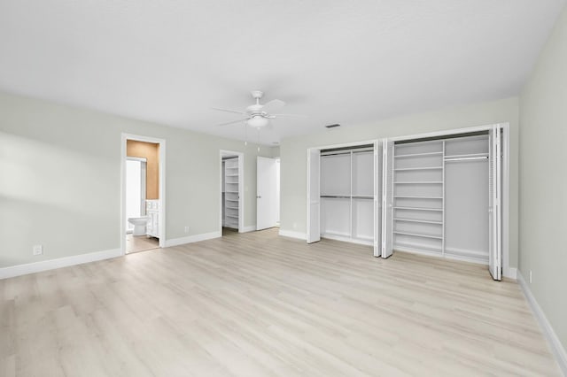 unfurnished bedroom with ceiling fan, ensuite bath, light hardwood / wood-style flooring, and two closets