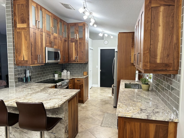 kitchen with a breakfast bar area, appliances with stainless steel finishes, light stone counters, tasteful backsplash, and a textured ceiling