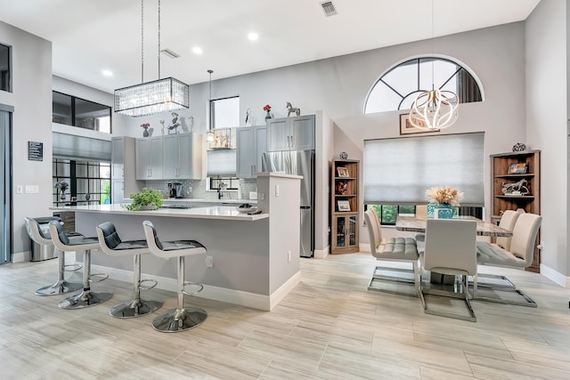 kitchen with gray cabinetry, a kitchen breakfast bar, decorative backsplash, hanging light fixtures, and an inviting chandelier