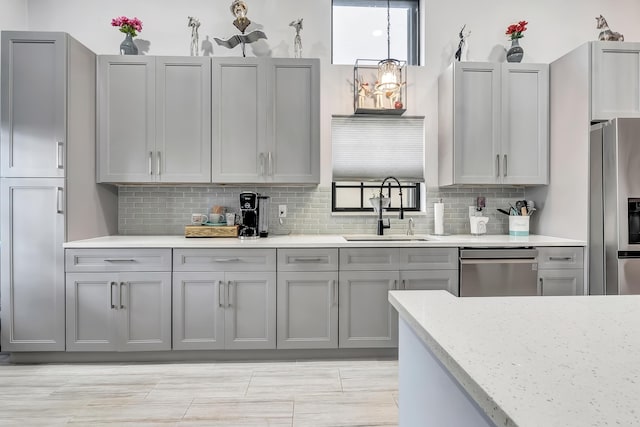 kitchen featuring sink, gray cabinetry, stainless steel appliances, light stone countertops, and backsplash