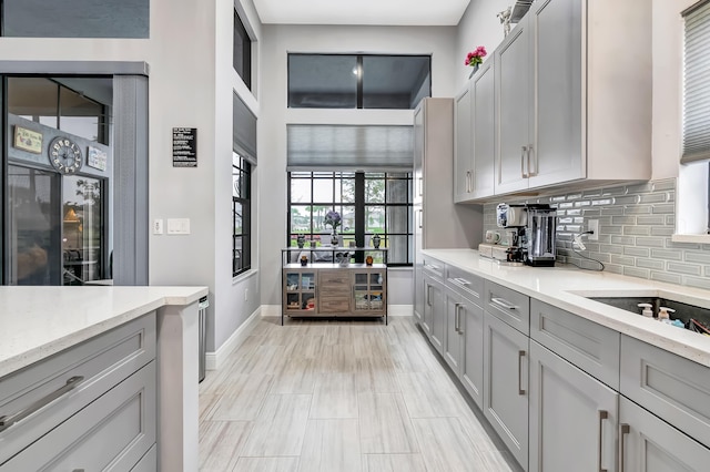 kitchen featuring light stone countertops, decorative backsplash, and gray cabinetry