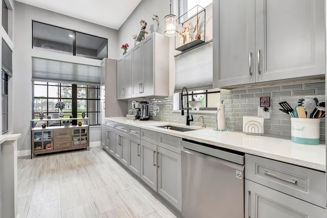 kitchen featuring sink, gray cabinetry, light stone counters, decorative backsplash, and stainless steel dishwasher