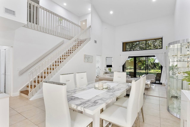 dining area featuring stairs, light tile patterned floors, a towering ceiling, and visible vents