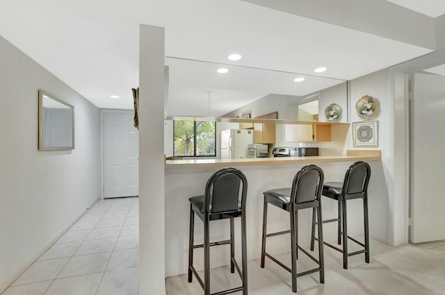 kitchen featuring a breakfast bar area, white fridge, light tile patterned flooring, kitchen peninsula, and light brown cabinets