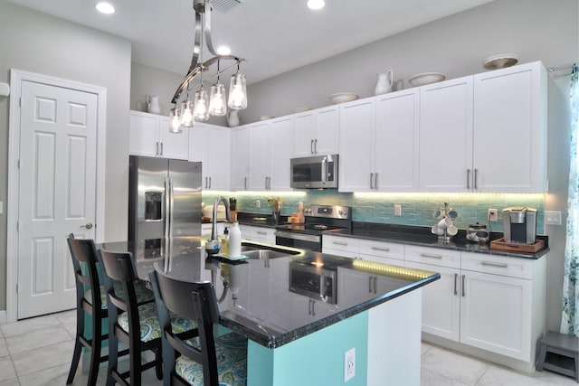 kitchen with stainless steel appliances, a center island with sink, and white cabinets