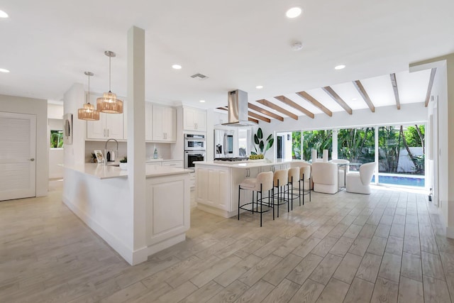 kitchen with double oven, white cabinetry, island range hood, a kitchen breakfast bar, and hanging light fixtures