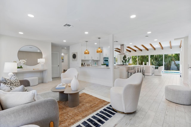 living room featuring light hardwood / wood-style flooring, sink, and beamed ceiling