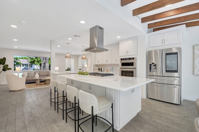 kitchen with appliances with stainless steel finishes, island exhaust hood, white cabinetry, decorative light fixtures, and a spacious island