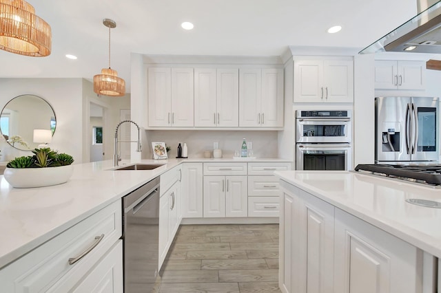 kitchen with sink, exhaust hood, white cabinetry, stainless steel appliances, and hanging light fixtures