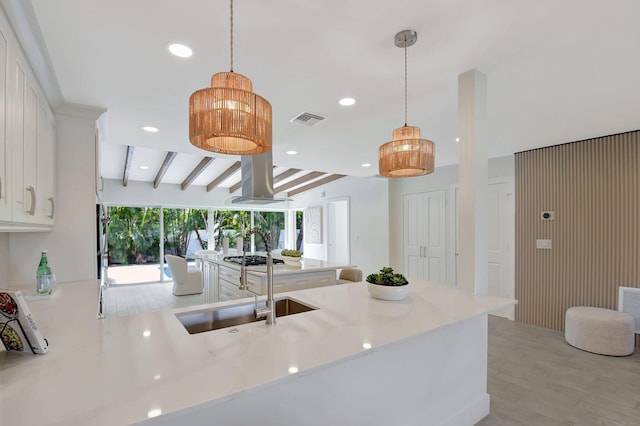 kitchen with hanging light fixtures, island range hood, white cabinetry, and sink