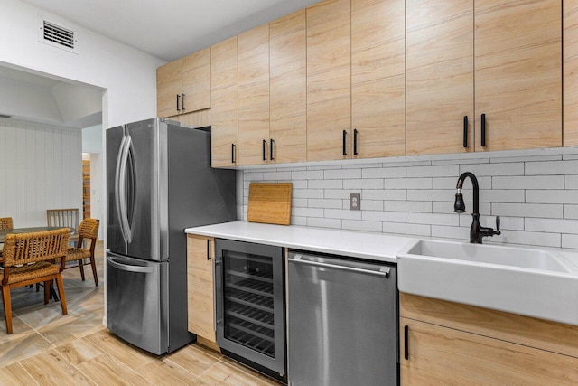 kitchen featuring sink, stainless steel appliances, light hardwood / wood-style floors, decorative backsplash, and beverage cooler