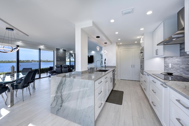 kitchen featuring decorative light fixtures, white cabinetry, a water view, light stone countertops, and wall chimney range hood