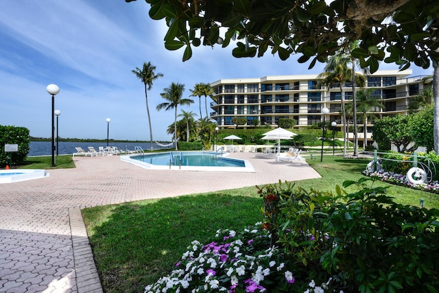 view of swimming pool with a patio, a water view, and a lawn