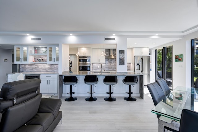 kitchen with a kitchen bar, wall chimney exhaust hood, white cabinets, and appliances with stainless steel finishes