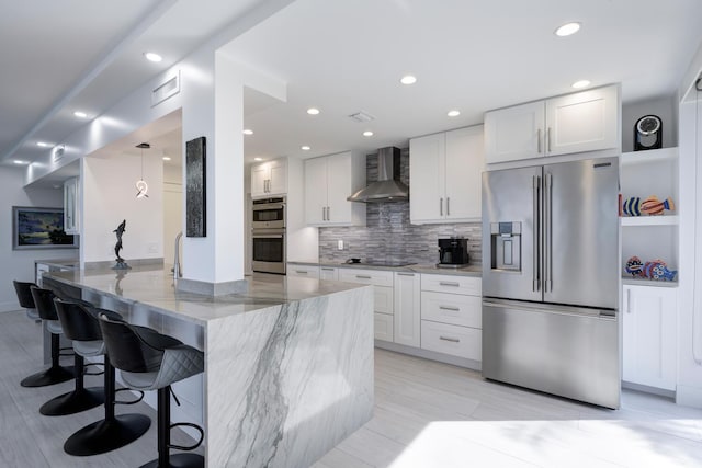 kitchen with stainless steel appliances, wall chimney range hood, white cabinets, and light stone counters