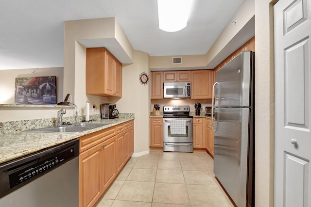 kitchen with light tile patterned floors, sink, stainless steel appliances, light stone counters, and light brown cabinets