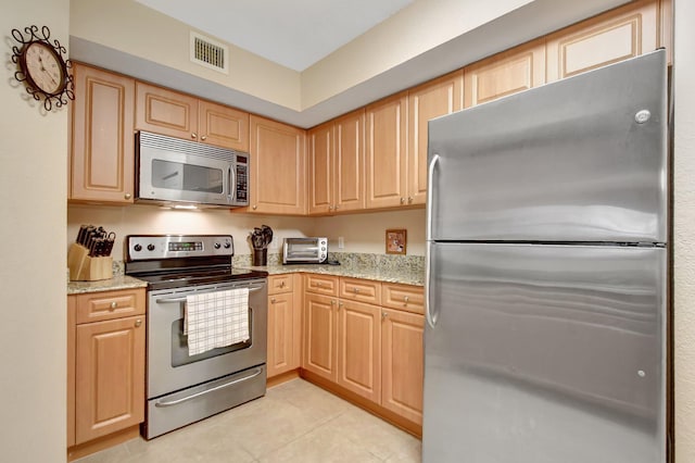 kitchen with light tile patterned flooring, appliances with stainless steel finishes, light brown cabinetry, and light stone counters