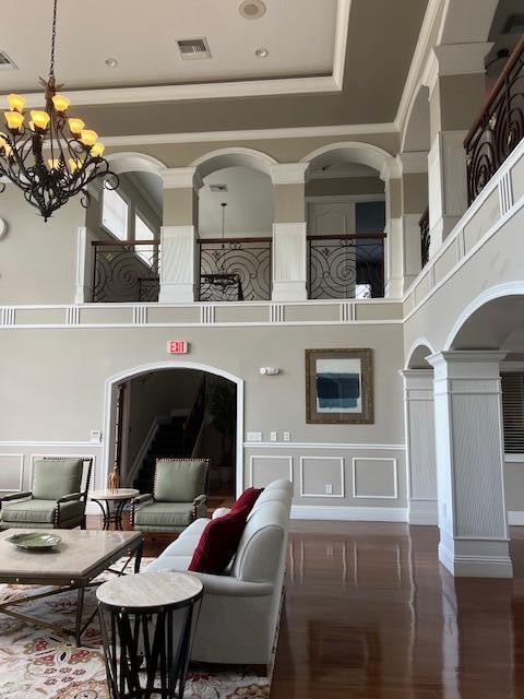 living room featuring an inviting chandelier, hardwood / wood-style floors, a towering ceiling, and decorative columns