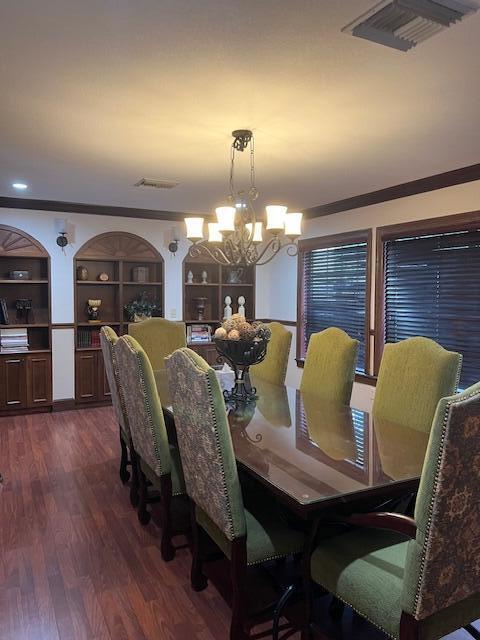 dining area with crown molding, dark hardwood / wood-style floors, a notable chandelier, and built in shelves