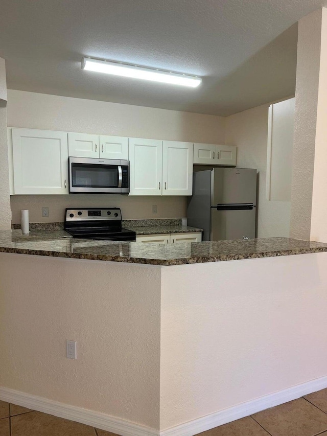 kitchen with white cabinetry, appliances with stainless steel finishes, tile patterned floors, and dark stone counters