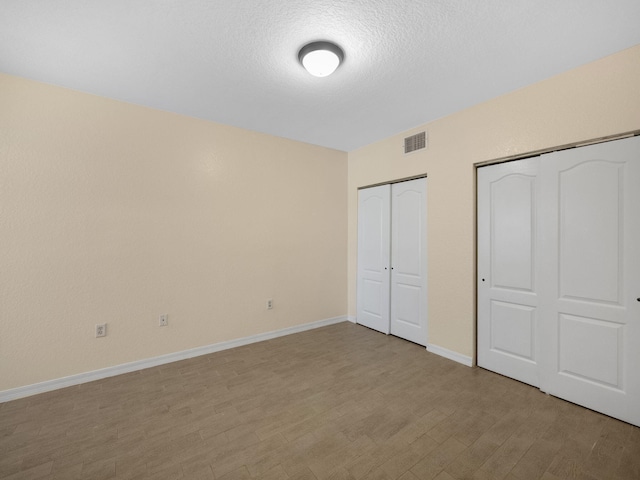 unfurnished bedroom featuring multiple closets, a textured ceiling, and light hardwood / wood-style floors