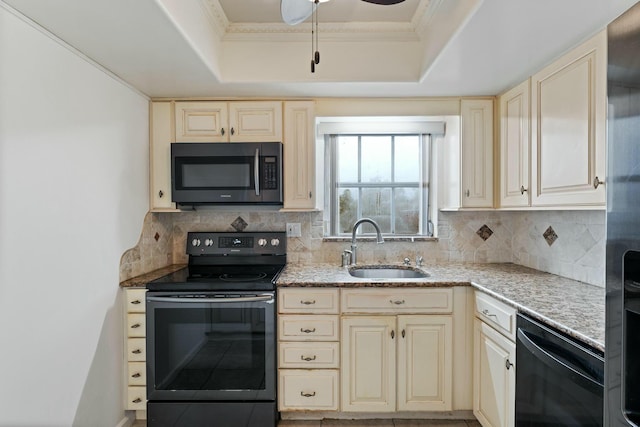 kitchen featuring sink, black appliances, a tray ceiling, cream cabinets, and backsplash