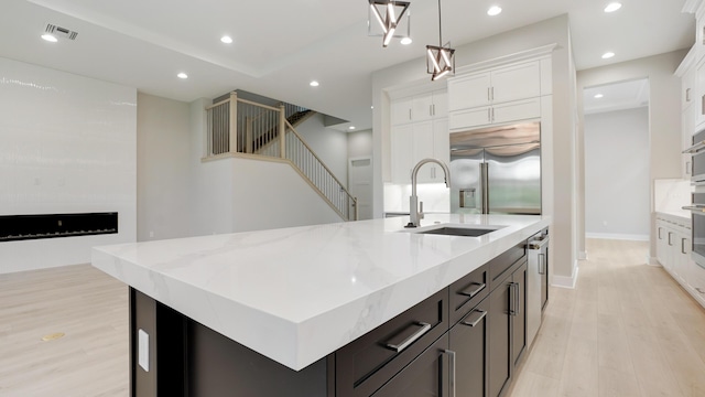 kitchen with sink, white cabinetry, decorative light fixtures, an island with sink, and stainless steel appliances