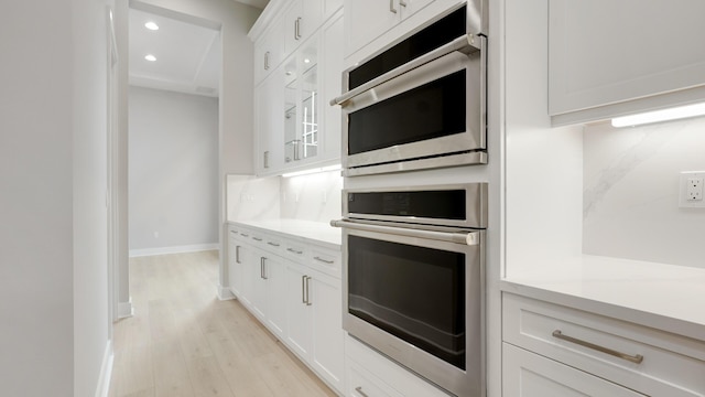 kitchen featuring white cabinetry, double oven, tasteful backsplash, and light wood-type flooring