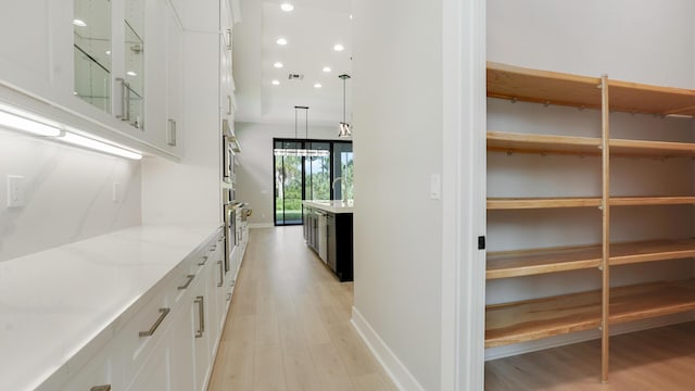 bar featuring hanging light fixtures, light stone countertops, oven, light hardwood / wood-style floors, and white cabinets