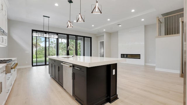 kitchen with sink, decorative light fixtures, an island with sink, stainless steel appliances, and a fireplace