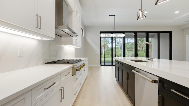 kitchen featuring sink, white cabinetry, hanging light fixtures, appliances with stainless steel finishes, and wall chimney range hood