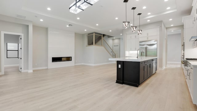 kitchen featuring stainless steel appliances, a center island with sink, white cabinets, and decorative light fixtures