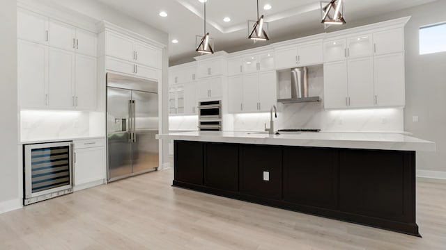 kitchen with pendant lighting, wall chimney range hood, stainless steel appliances, a center island with sink, and beverage cooler