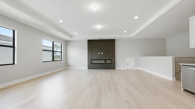 unfurnished living room featuring a tray ceiling, plenty of natural light, light hardwood / wood-style floors, and a large fireplace