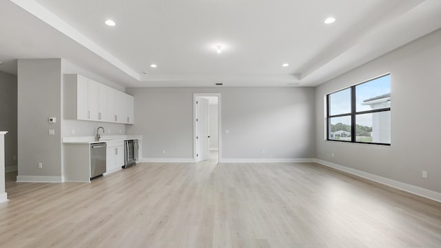 unfurnished living room featuring beverage cooler, a raised ceiling, and light wood-type flooring