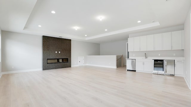 unfurnished living room with a tray ceiling, light hardwood / wood-style floors, and beverage cooler