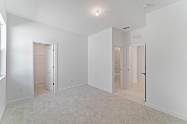 unfurnished bedroom with ensuite bathroom, a textured ceiling, light carpet, a spacious closet, and a closet