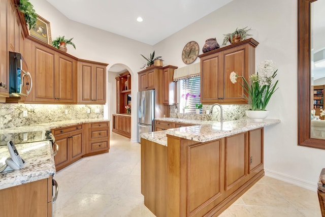 kitchen featuring stainless steel appliances, backsplash, light stone counters, and kitchen peninsula