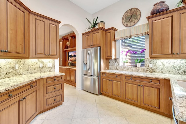 kitchen featuring stainless steel refrigerator with ice dispenser, tasteful backsplash, light stone counters, and light tile patterned floors