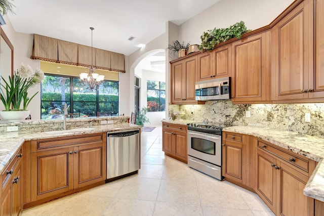 kitchen with sink, decorative light fixtures, appliances with stainless steel finishes, light stone countertops, and backsplash